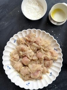 Raw chicken pieces coated with cornstarch, seasonings, and olive oil in a bowl.
