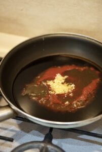 A skillet containing dark sauce, red chili sauce, and minced garlic before stirring.