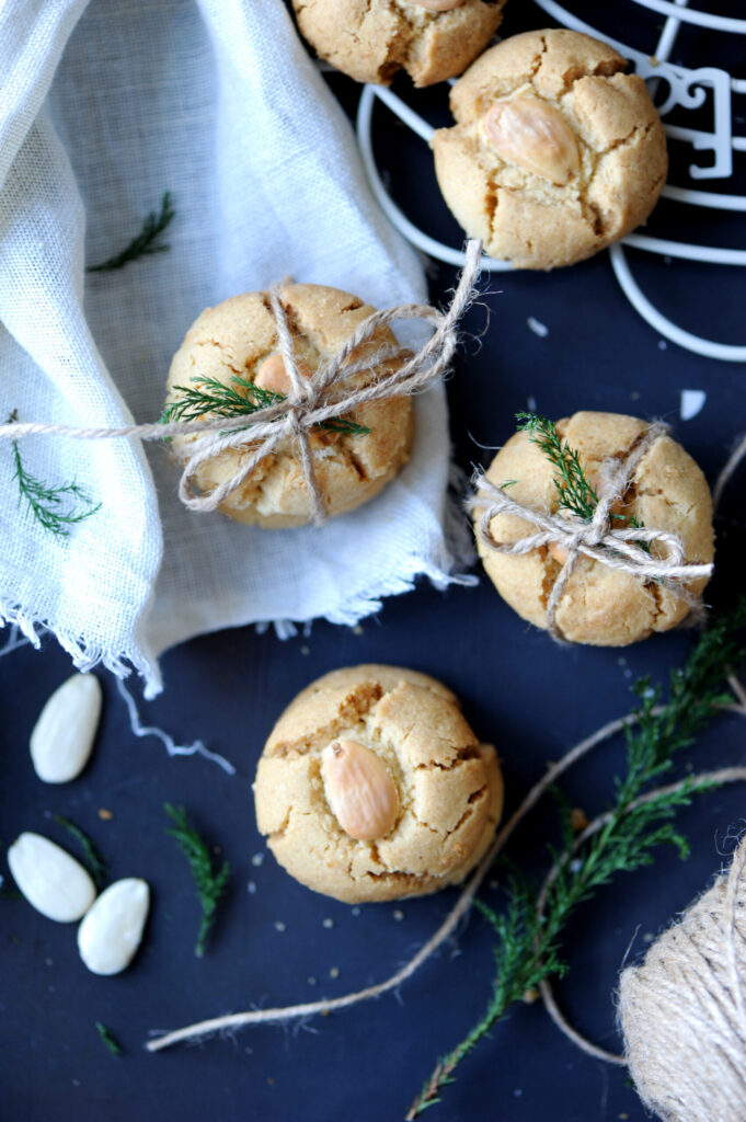 Almond-topped tahini cookies styled with twine and greenery beside a white cloth.