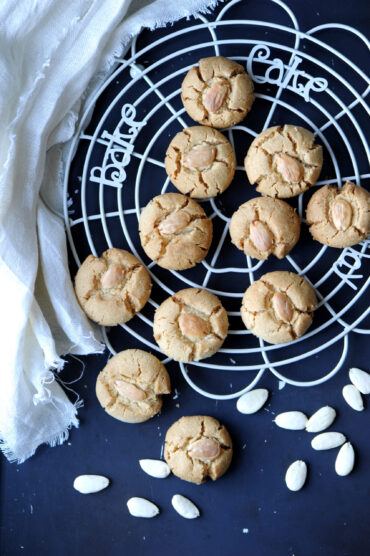 Overhead view of tahini cookies topped with whole almonds on a white cooling rack.